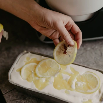 A hand scooping lemon curd ice cream from a container.