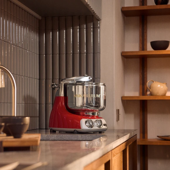Ankarsrum Assistent Original in Red on a kitchen countertop in a warm kitchen with wooden details.