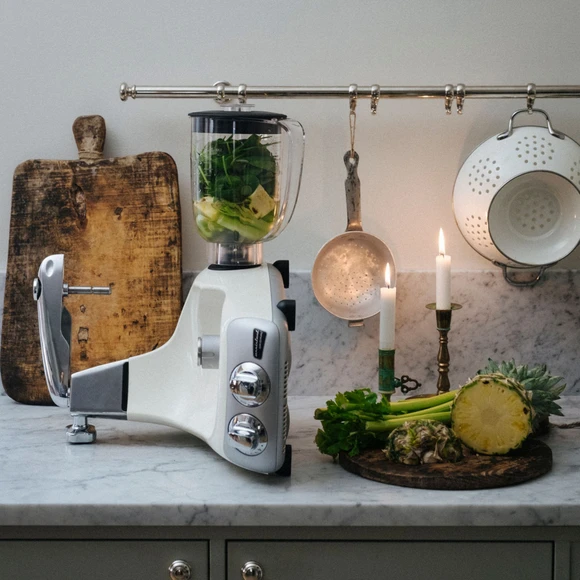 Ankarsrum Assistent Original med blenderen monteret, med grønne grøntsager og ananas i blenderen og ved siden af på en køkkenbordplade i marmor.