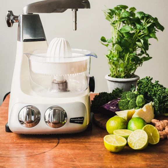 Ankarsrum Assistent Original with the Citrus Press attached. Colorful vegetables and citrus fruits beside it.