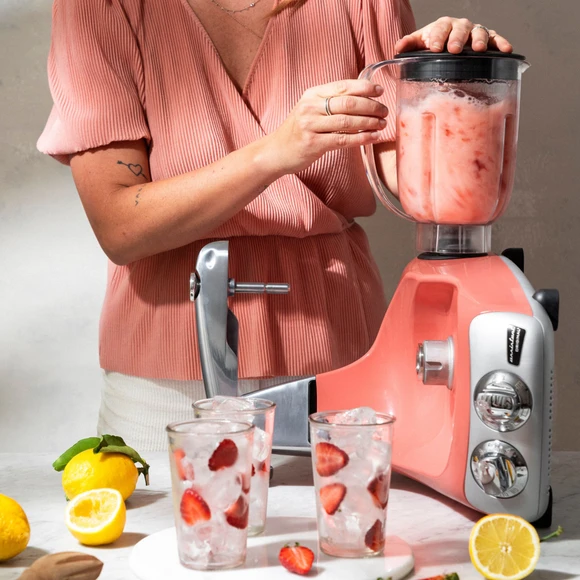 Ankarsrum Assistent Original con il frullatore montato, mentre prepara una limonata, con una persona sullo sfondo e limoni e bicchieri con ghiaccio e fragole accanto.