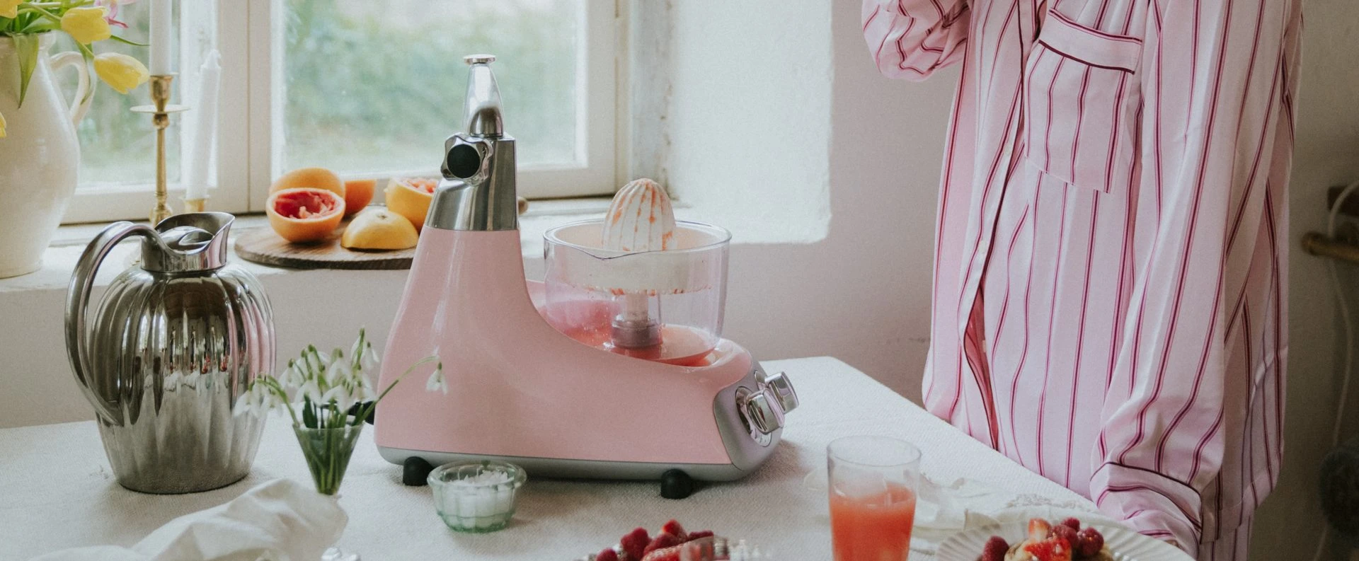 Frisch gepresster Saft mit dem Zitruspressen-Aufsatz auf der rosa Ankarsrum Küchenmaschine in der Farbe Cloudy Pink – für einen gesunden Start in den Tag.