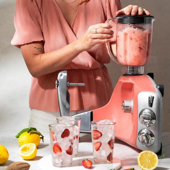 Ankarsrum Assistent Original con il frullatore montato, mentre prepara una limonata, con una persona sullo sfondo e limoni e bicchieri con ghiaccio e fragole accanto.