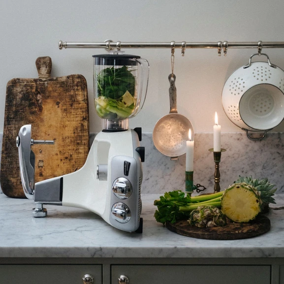Ankarsrum Assistent Original avec le mélangeur installé, avec des légumes verts et de l’ananas dans le mélangeur et à côté, sur un comptoir de cuisine en marbre.