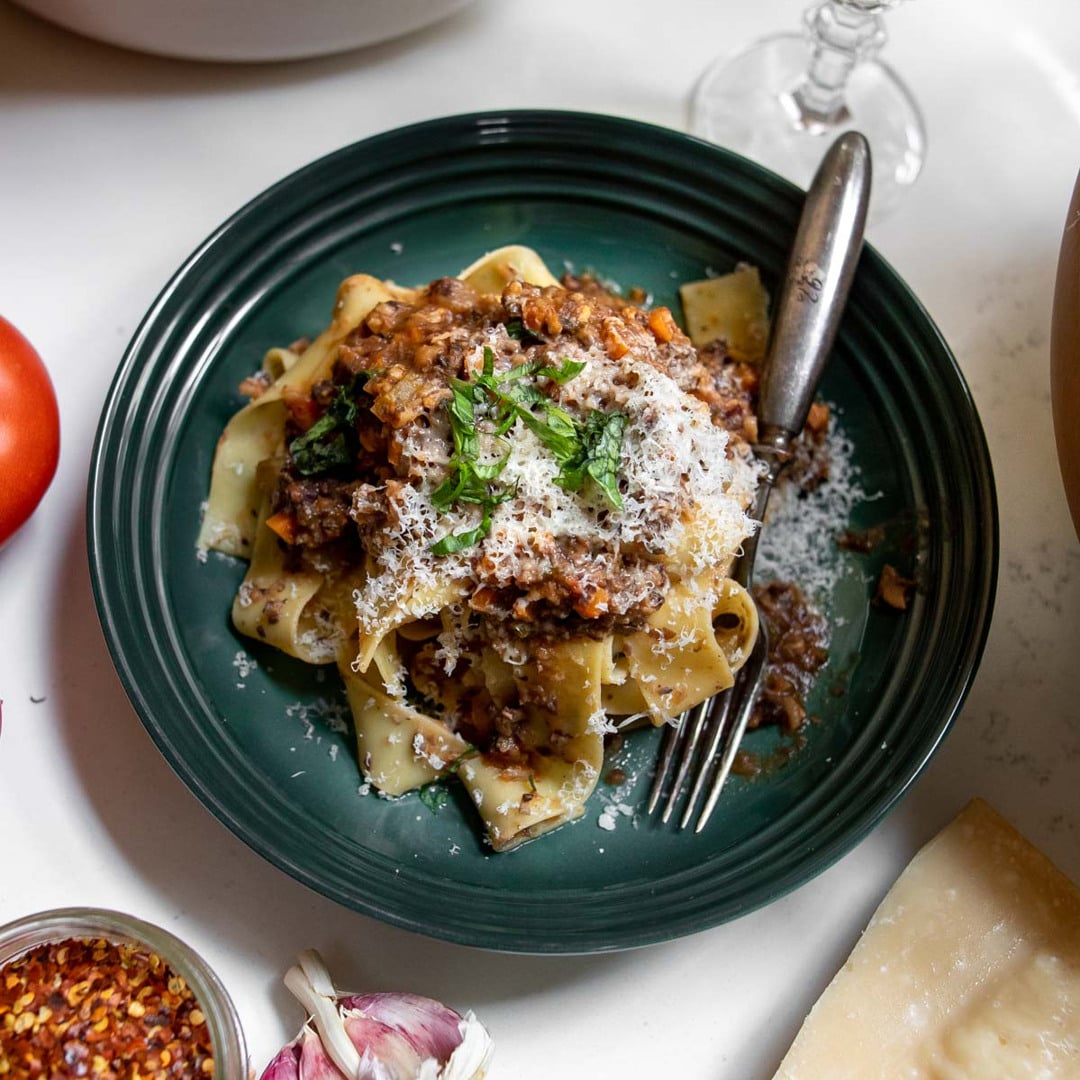 En tallerken med frisk pasta serveret med svampebolognese, revet parmesan og friske krydderurter.